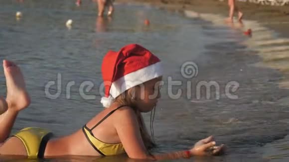 戴着红色圣诞帽的小可爱女孩在海滩上玩得很开心视频的预览图