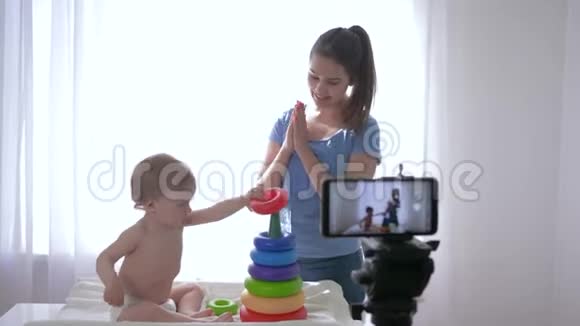 Videoblog婴儿男孩和妇女一起玩教育玩具在手机直播中录制社交媒体视频视频的预览图