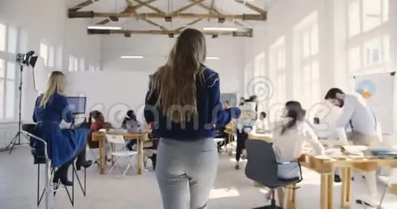 镜头跟随金发女性助理经理携带咖啡在现代多民族光办公室的合伙人会议视频的预览图