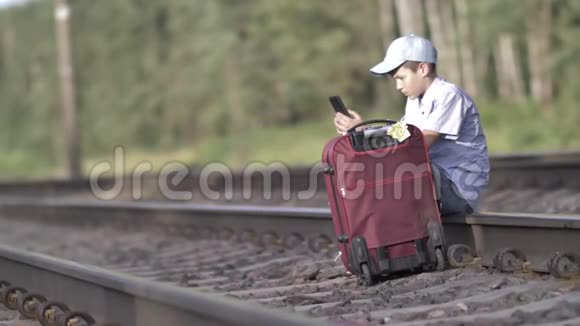 悲伤而愤怒的旅行者男孩在铁路上看电话里的信息视频的预览图