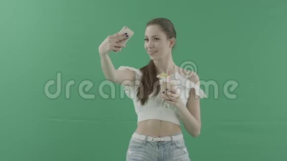 年轻性感的女人在绿色背景下用鸡尾酒拍照视频的预览图