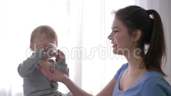 第一个孩子成功了快乐的男孩独立地喝矿泉水从旁边的玻璃到年轻的微笑的母亲视频的预览图