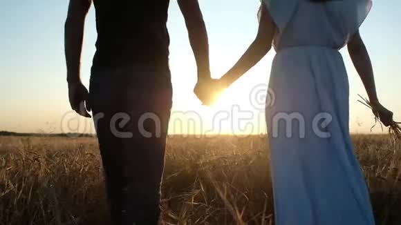 一对恋爱中的男人和一个女人在五彩缤纷的夏日日落中走在麦田里视频的预览图