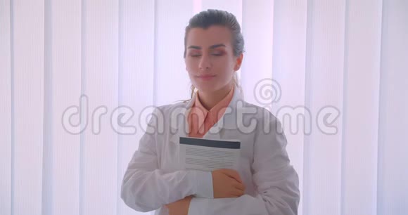 年轻迷人的白种人女医生拿着一本书看着镜头微笑的特写照片视频的预览图