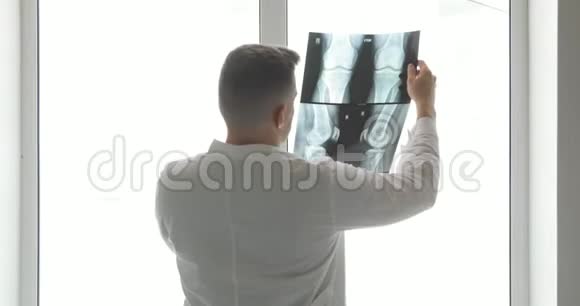 骨科医生在靠近窗户的x光图像上诊断骨骼的损伤后视视频的预览图