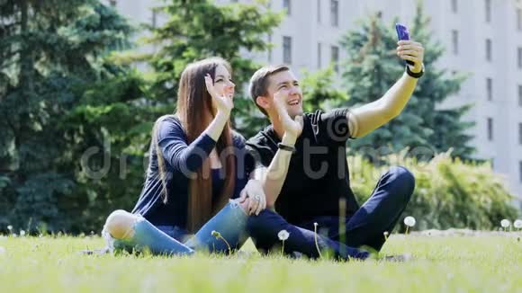 快乐的年轻夫妇通过手机在视频聊天坐在公园的草地上通过视频与朋友交谈视频的预览图