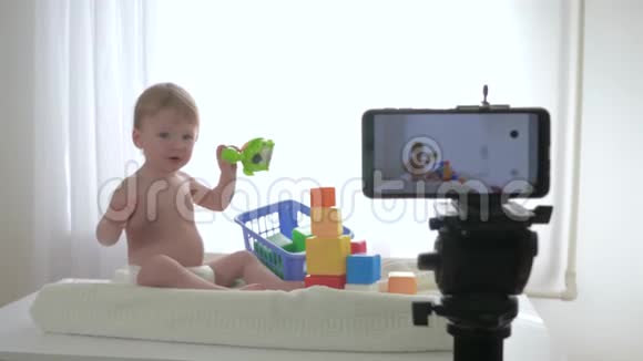 博客快乐微笑的小男孩正在玩玩具和拍手同时在网上写流媒体直播视频的预览图