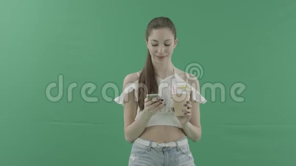 性感的年轻女人一边喝鸡尾酒一边在智能手机上上网一边对着绿色的相机视频的预览图