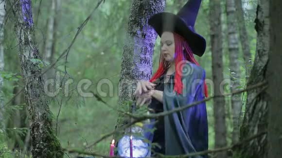 一个红头发黑帽子黑斗篷的年轻女巫正在森林里施展魔法视频的预览图