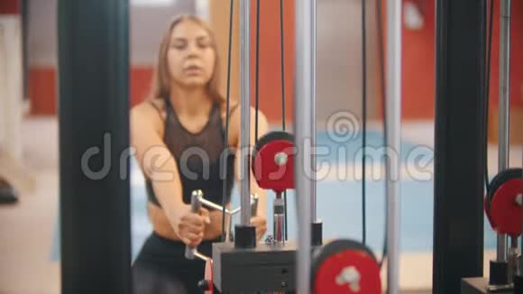 一位运动服的运动员女士在健身房训练把手柄拉到重量块上视频的预览图