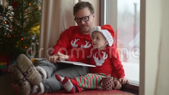 父亲和他的小儿子在舒适的客厅里看书假日的家庭时间视频的预览图
