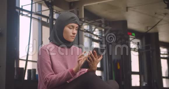 用平板电脑拍摄穆斯林年轻年轻女性在头巾上的特写照片并在健身房中显示绿色彩色屏幕视频的预览图