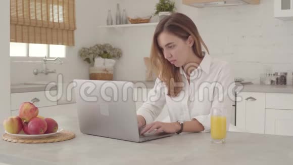 年轻的白人女商人坐在桌子旁在笔记本电脑上打字穿白色衬衫的漂亮女孩在网上工作视频的预览图