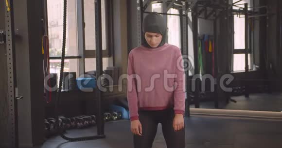 年轻有魅力的穆斯林女性在室内健身房用哑铃做蹲像特写视频的预览图