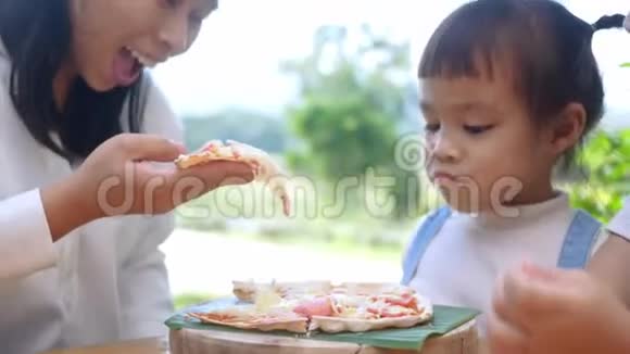 可爱的饥饿的女孩喜欢在后院和妈妈一起吃自制的披萨有家人的小女孩在户外的午餐桌上视频的预览图