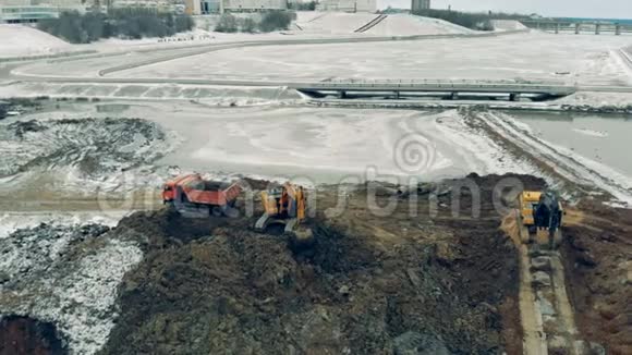 从建筑工地上方的空中俯瞰挖掘机和卡车在工作机器在一个大事业中工作视频的预览图