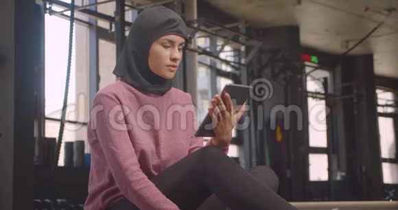用平板电脑拍摄穆斯林年轻年轻女性戴头巾的特写照片并在室内健身房拍摄绿色屏幕视频的预览图