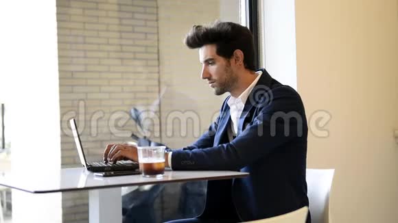 商人坐在咖啡馆里用他的笔记本电脑喝着新鲜的咖啡打字视频的预览图