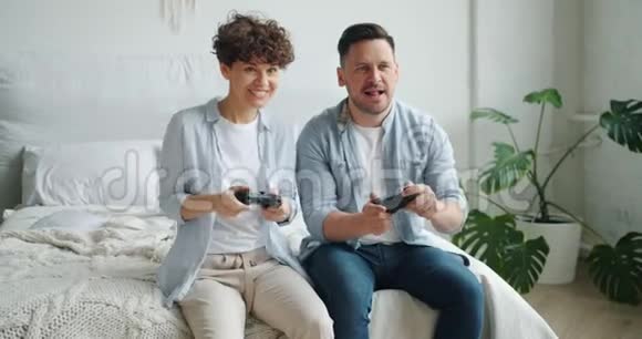 可爱的情侣男女朋友坐在卧室的床上玩电子游戏视频的预览图