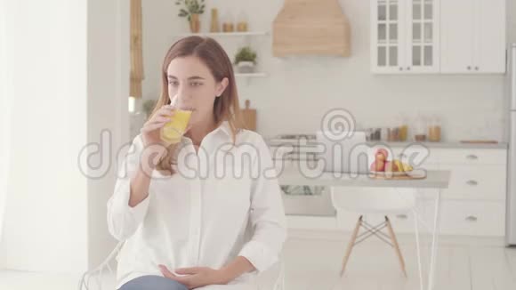 一位年轻漂亮的高加索女人坐在轻盈的现代厨房里喝橙汁的肖像很漂亮的笑容视频的预览图