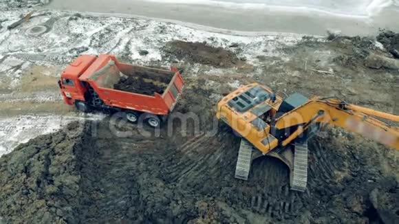 从建筑工地上方的空中俯瞰挖掘机和卡车在工作一个装载机把石头和沙子放进视频的预览图