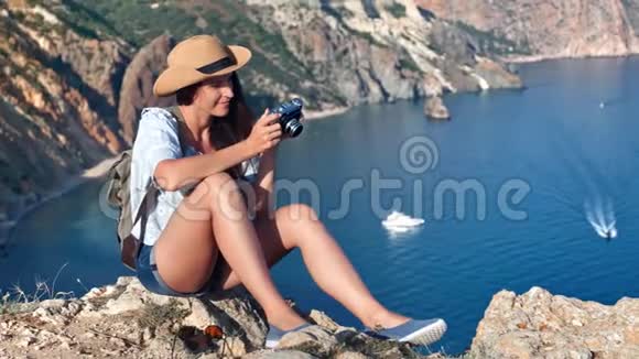 快乐的女游客坐在山顶上在海港拍照视频的预览图