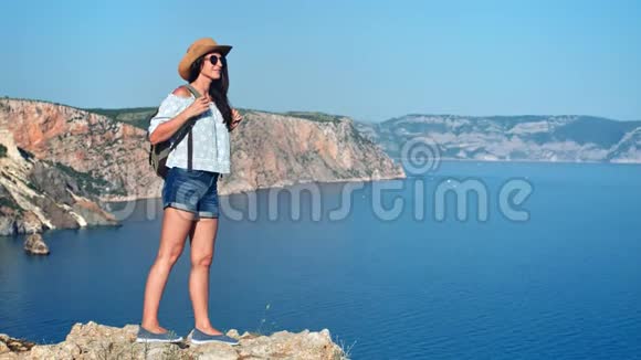 迷人的旅行背包客女人站在山顶欣赏美丽的海洋景观视频的预览图