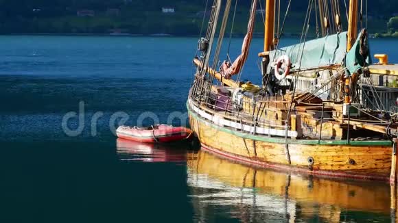 漂浮在水面上的充气红色橡皮艇筏用绳子系在木帆船的栏杆上视频的预览图