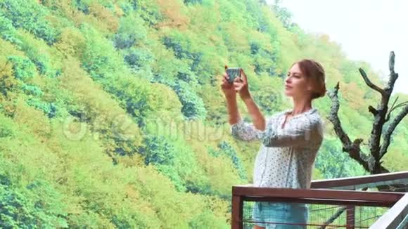 可爱的女孩金发碧眼的辫子在她的新手机上制作了高质量的照片她的新手机在悬崖上的空中桥奥卡塞斯峡谷视频的预览图