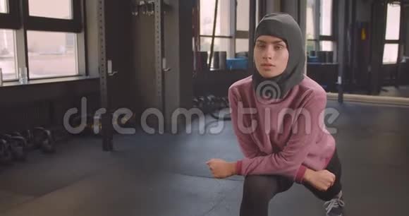 年轻坚定的穆斯林女性戴着头巾在健身房室内伸展的特写照片视频的预览图