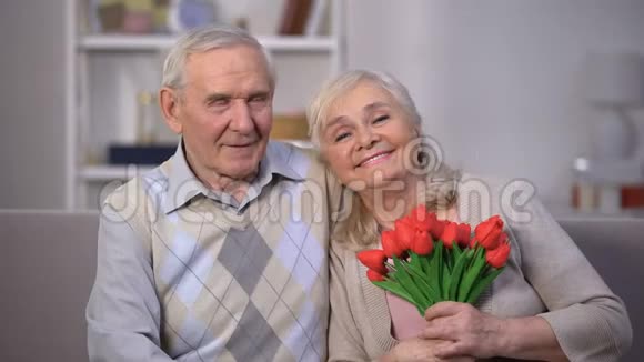 一对老夫妇在家拥抱一个女人拿着一束郁金香结婚纪念日礼物视频的预览图