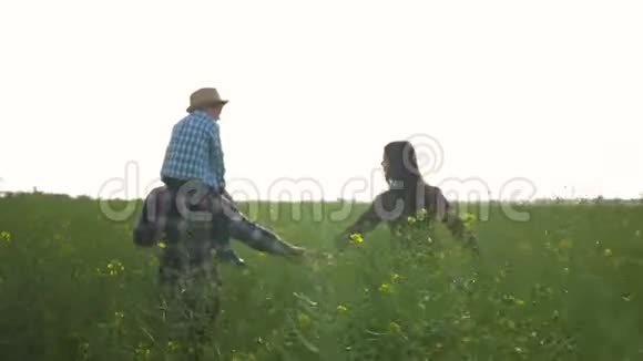 农场快乐的男孩子肩上扛着小男孩女孩子在绿色的油菜田里与天空并肩行走视频的预览图