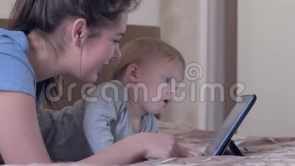 现代家庭休闲有着年轻妈妈的好孩子躺在家里的床上玩触摸片视频的预览图