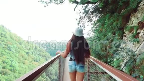 可爱的女孩长着一头直黑色的长发走在Okatce峡谷上的木桥上运动的女士她的头发和头发都挺直了视频的预览图