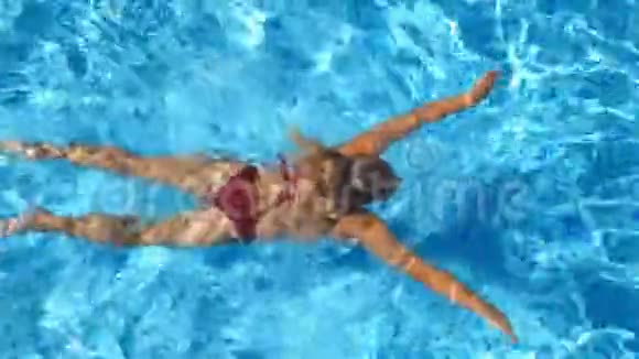 无法辨认的美丽女孩穿着红色比基尼漂浮在酒店的游泳池上年轻女子在清澈的蓝水中游泳视频的预览图