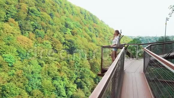 年轻女子穿着浅白色波尔卡DOT上衣和牛仔短裤在Okatse峡谷的桥上与视频的预览图