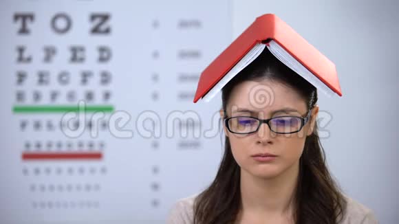 女士头上拿着书看着摄像机过度劳累的学生准备考试视频的预览图