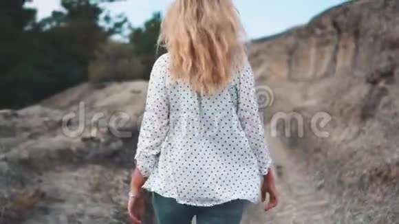 自信的女孩一头轻盈飘逸的金发沿着石山的小路走着迎接命运女士挺直了腰板视频的预览图