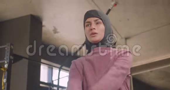 年轻的运动穆斯林女性戴着头巾在健身房里用哑铃做蹲像特写视频的预览图