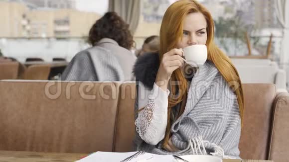 年轻的白种人女人被覆盖在毯子上喝茶或咖啡坐在露台上的桌子上女孩喜欢视频的预览图