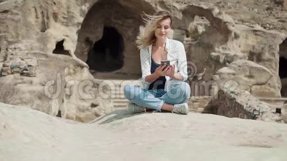 一个女人坐在石头上打电话查看邮件自由职业者从世界各个角落工作视频的预览图