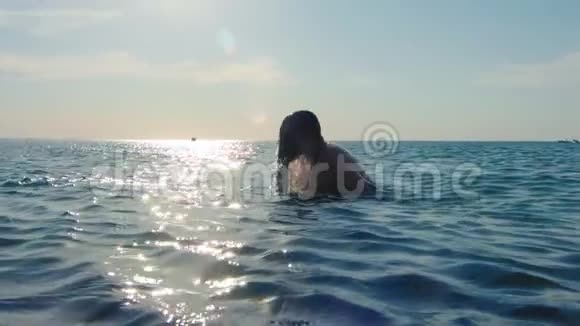 强壮的男人沐浴在大海中在日落时分玩长发周围是飞溅的慢动作视频的预览图