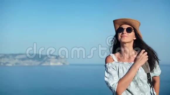 微笑着旅行的女人戴着帽子戴着太阳镜在山顶上走过海中射击视频的预览图