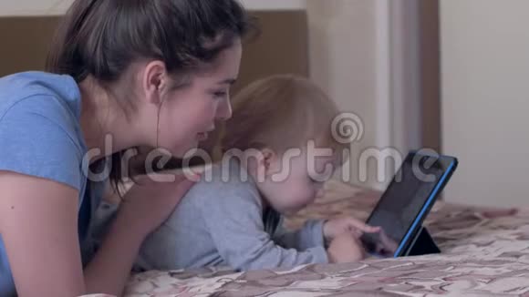 教育技术好奇的男孩和快乐的妈妈玩数字平板电脑躺在房间的床上视频的预览图