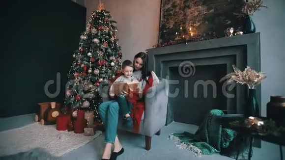 美丽的妈妈和儿子在圣诞树附近读童话视频的预览图