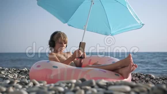可爱的儿童在沙滩上用智能手机听音乐视频的预览图