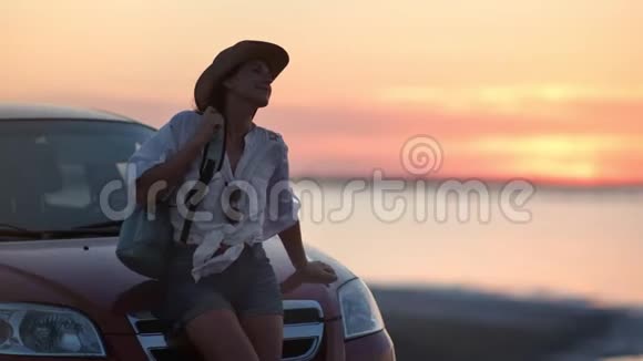 可爱的年轻旅游妇女在车帽上放松挥舞着头发享受黄昏的日落海景视频的预览图