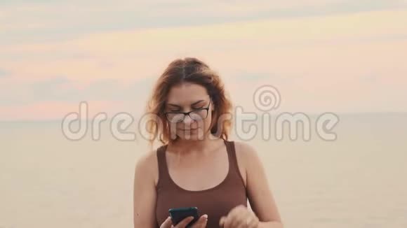 美丽可爱的年轻女子在佐治亚州海边的绚丽夜空中女士拿着手机对着镜头微笑视频的预览图