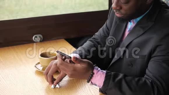 黑人商人用耳机听音乐坐在咖啡馆里喝咖啡视频的预览图