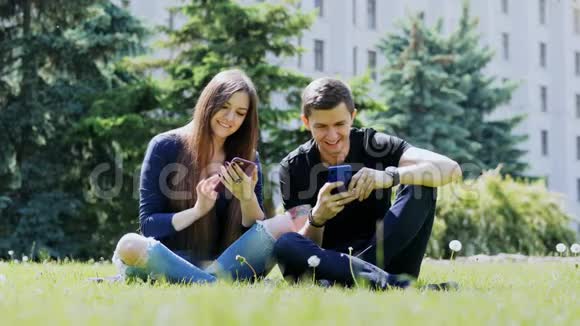 快乐的朋友在草地上的城市公园里玩手机聊天视频的预览图
